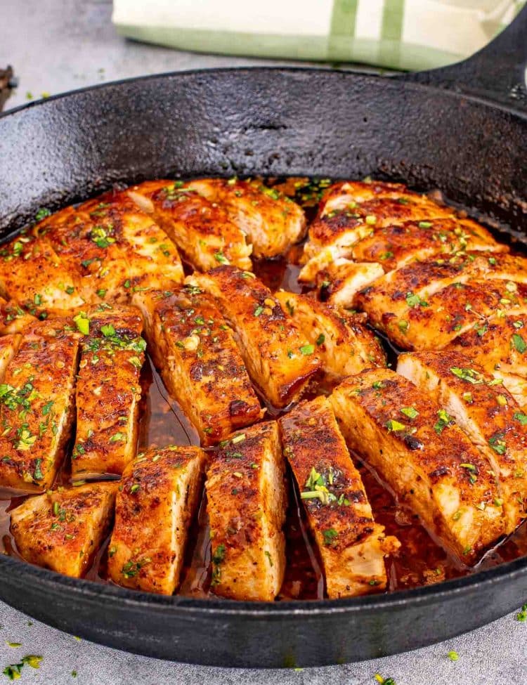 Close-up of juicy chicken breasts simmering in a cast iron skillet with glossy garlic butter sauce and fresh parsley.