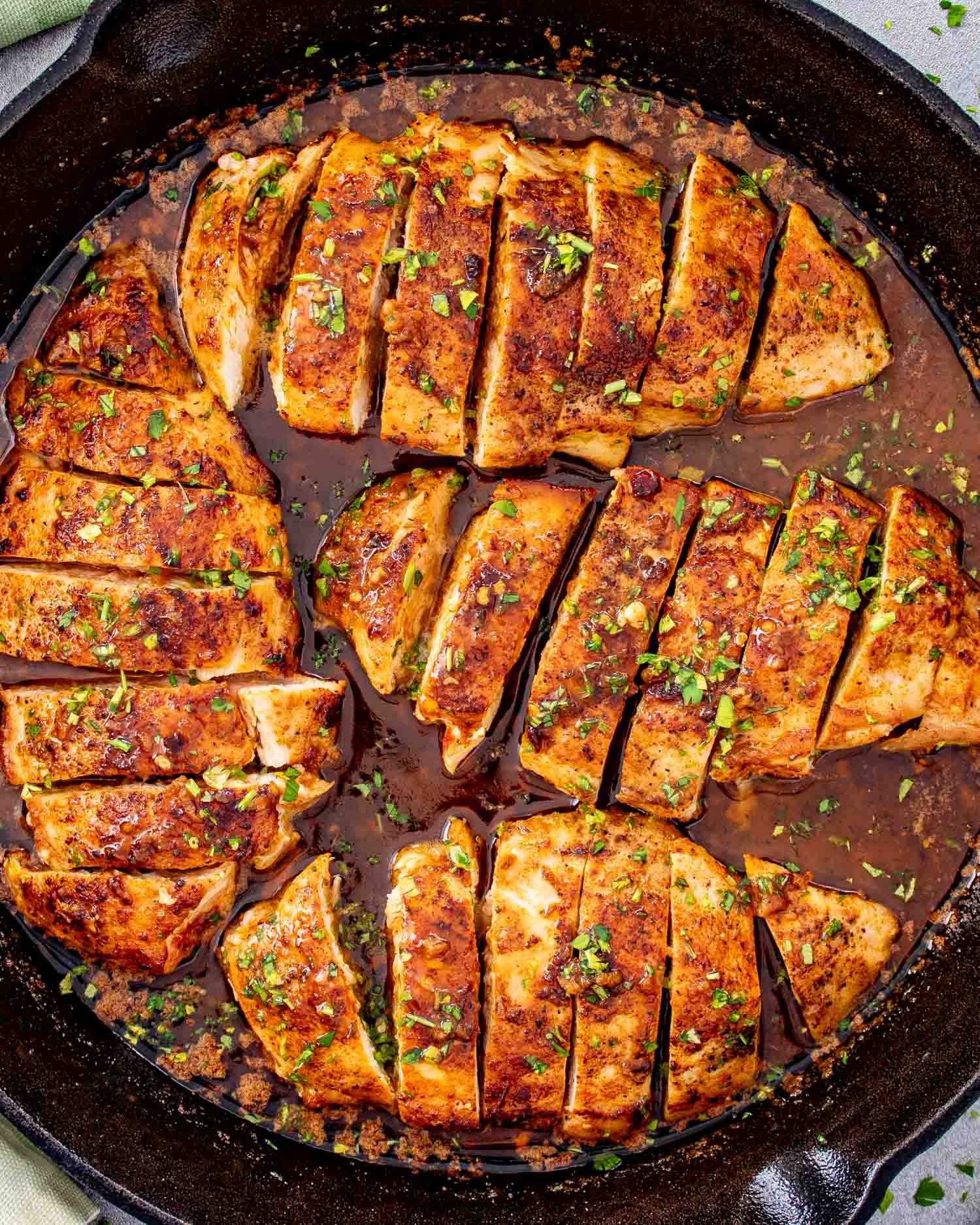 Pan-seared chicken breasts sliced and arranged in a skillet, covered in rich cowboy butter sauce with herbs and spices.