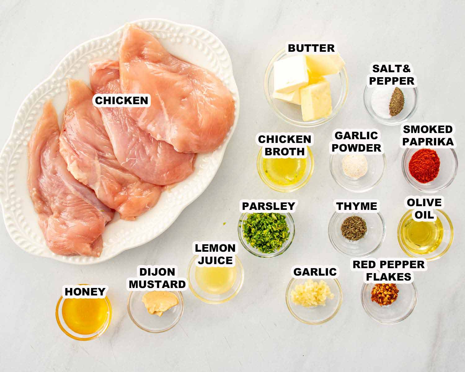 Raw chicken breasts with labeled ingredients including butter, garlic, Dijon, honey, lemon juice, and spices arranged on a light surface.