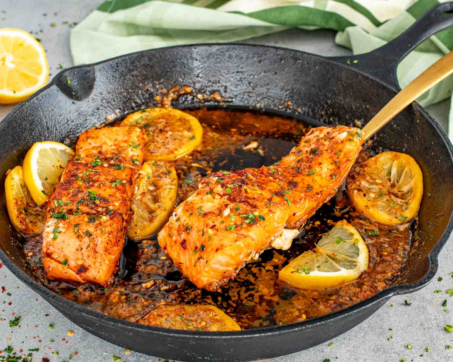 Crispy salmon fillets cooking in skillet with lemon slices and glossy cowboy butter sauce.