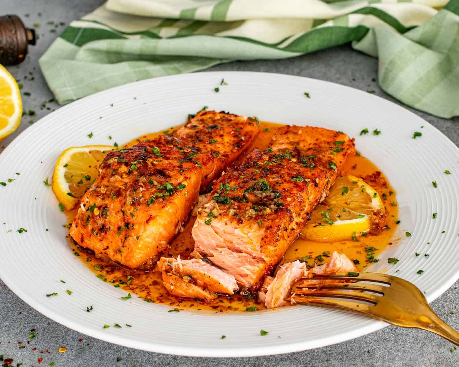 Flaky cowboy butter salmon fillet on plate with lemon slices and rich garlic butter sauce.