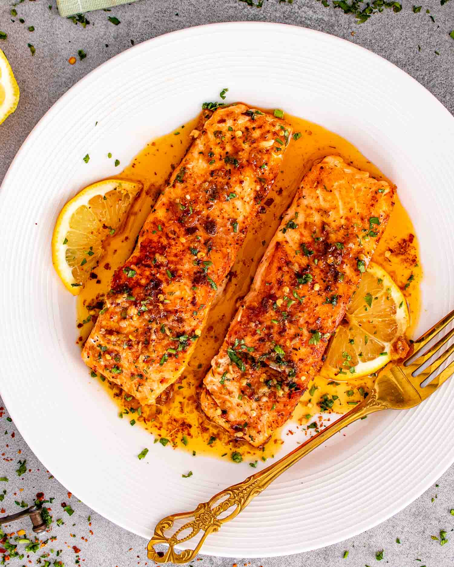 Cowboy butter salmon fillets served on white plate with lemon slices and rich garlic butter sauce.