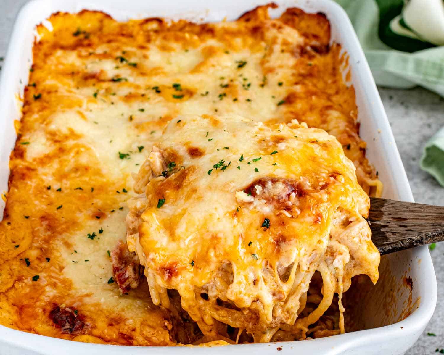 Creamy baked spaghetti with melted mozzarella being lifted from baking dish.