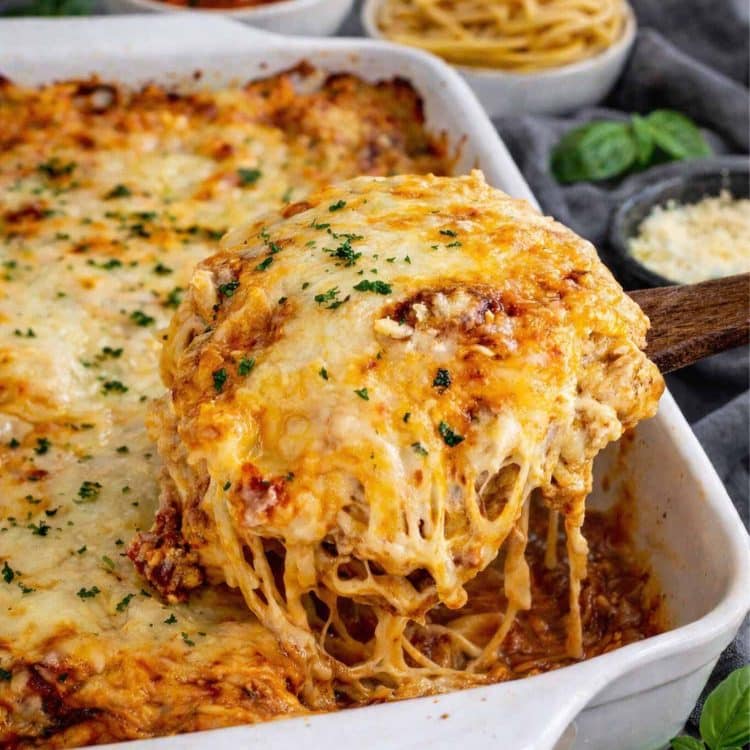 Creamy baked spaghetti with melted mozzarella being lifted from baking dish.