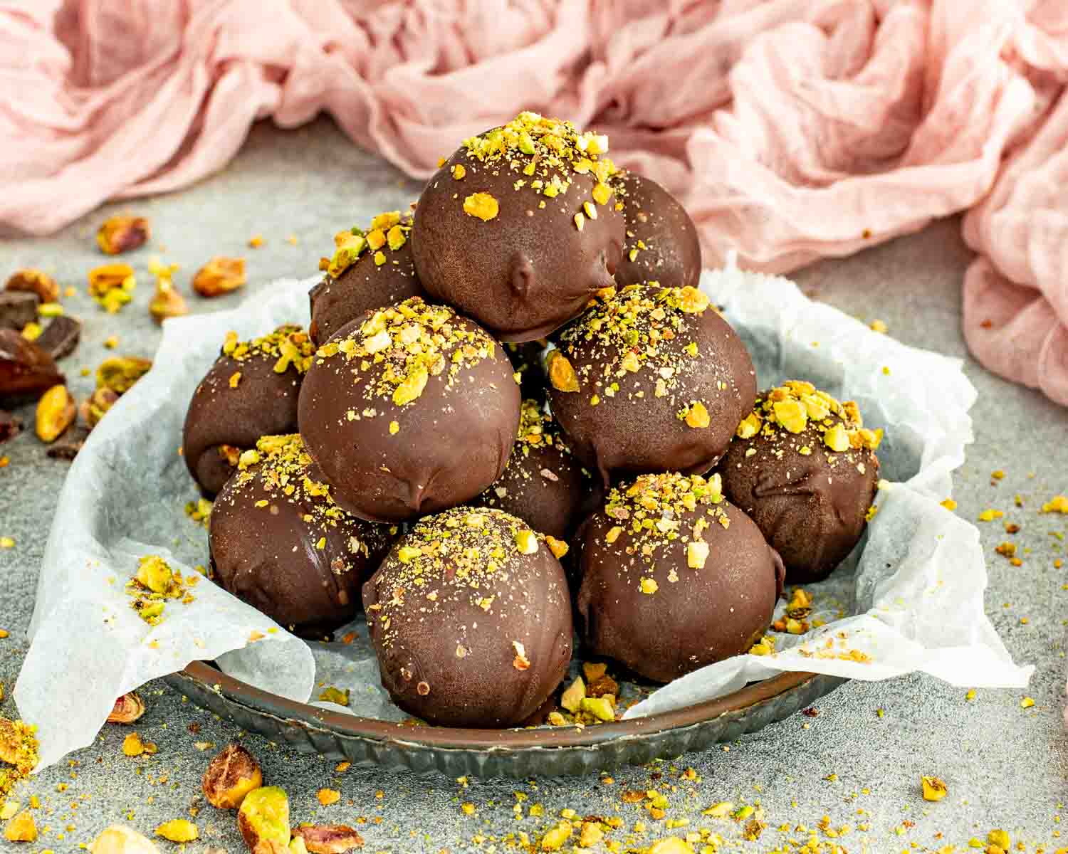 No bake pistachio date chocolate balls coated in dark chocolate on a plate.