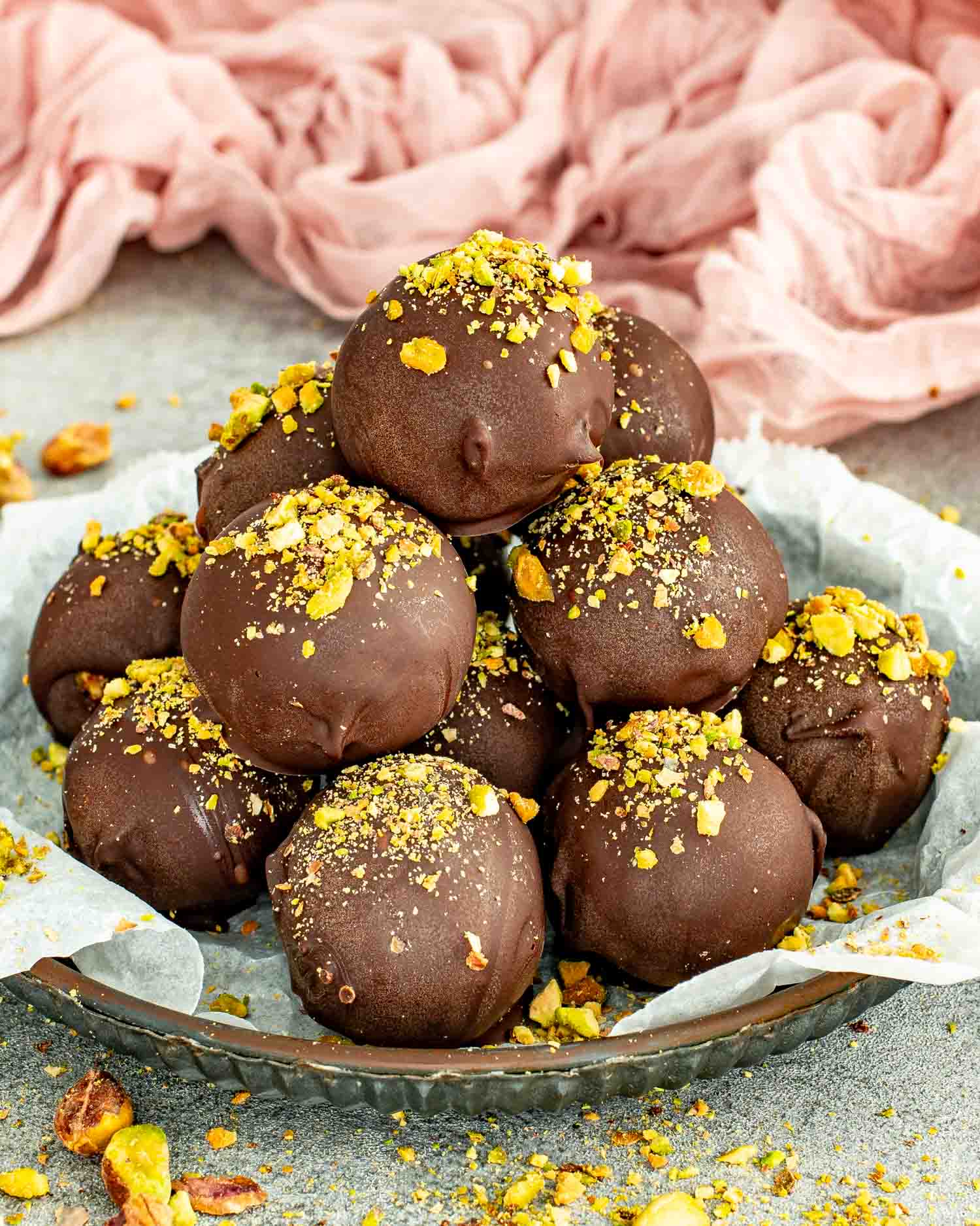Easy pistachio date chocolate balls garnished with chopped pistachios on a plate.