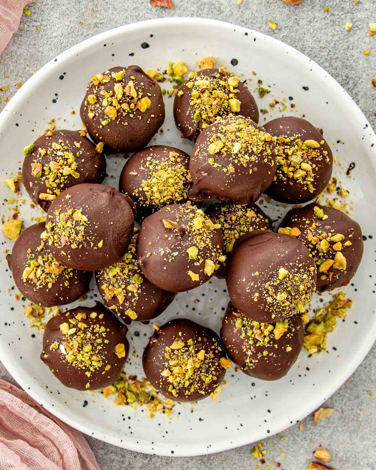 Pistachio date chocolate balls topped with chopped pistachios on a white plate.