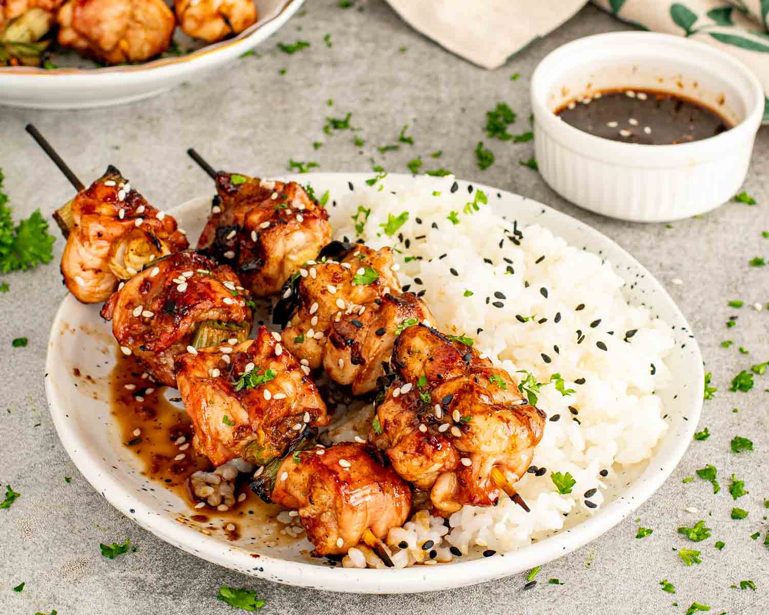 A side view of a chicken and green onion skewer being served with rice showing the glossy texture of the homemade yakitori sauce.