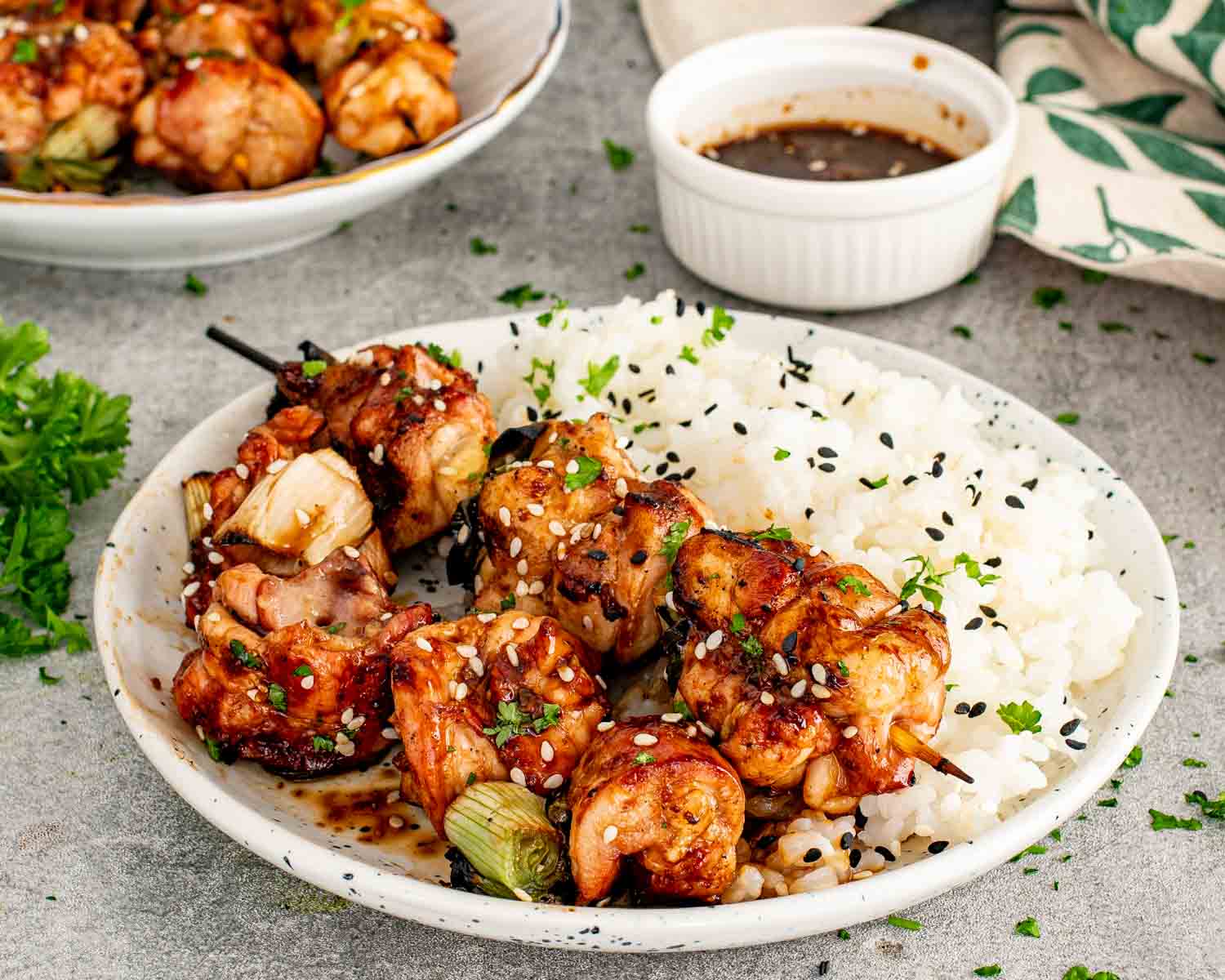 A finished plate of Japanese chicken skewers served with fluffy white rice and a small white bowl of extra tare dipping sauce.