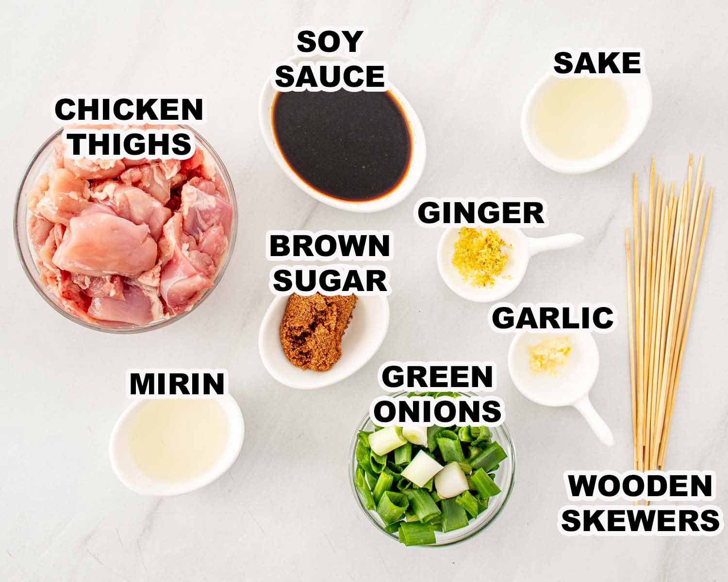 Overhead view of ingredients for Chicken Yakitori including raw chicken thighs, green onions, soy sauce, mirin, sake, brown sugar, ginger, garlic, and wooden skewers all labeled with clean black text.