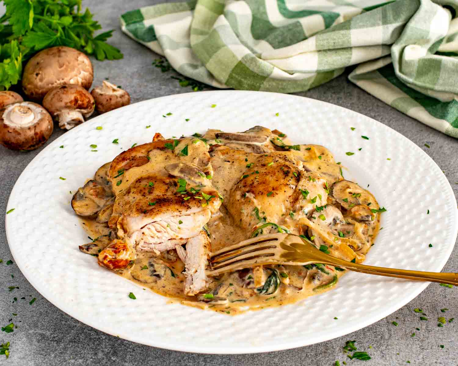 Creamy mushroom and sun dried tomato chicken served on white plate with golden seared chicken, mushrooms, spinach, and rich creamy sauce.