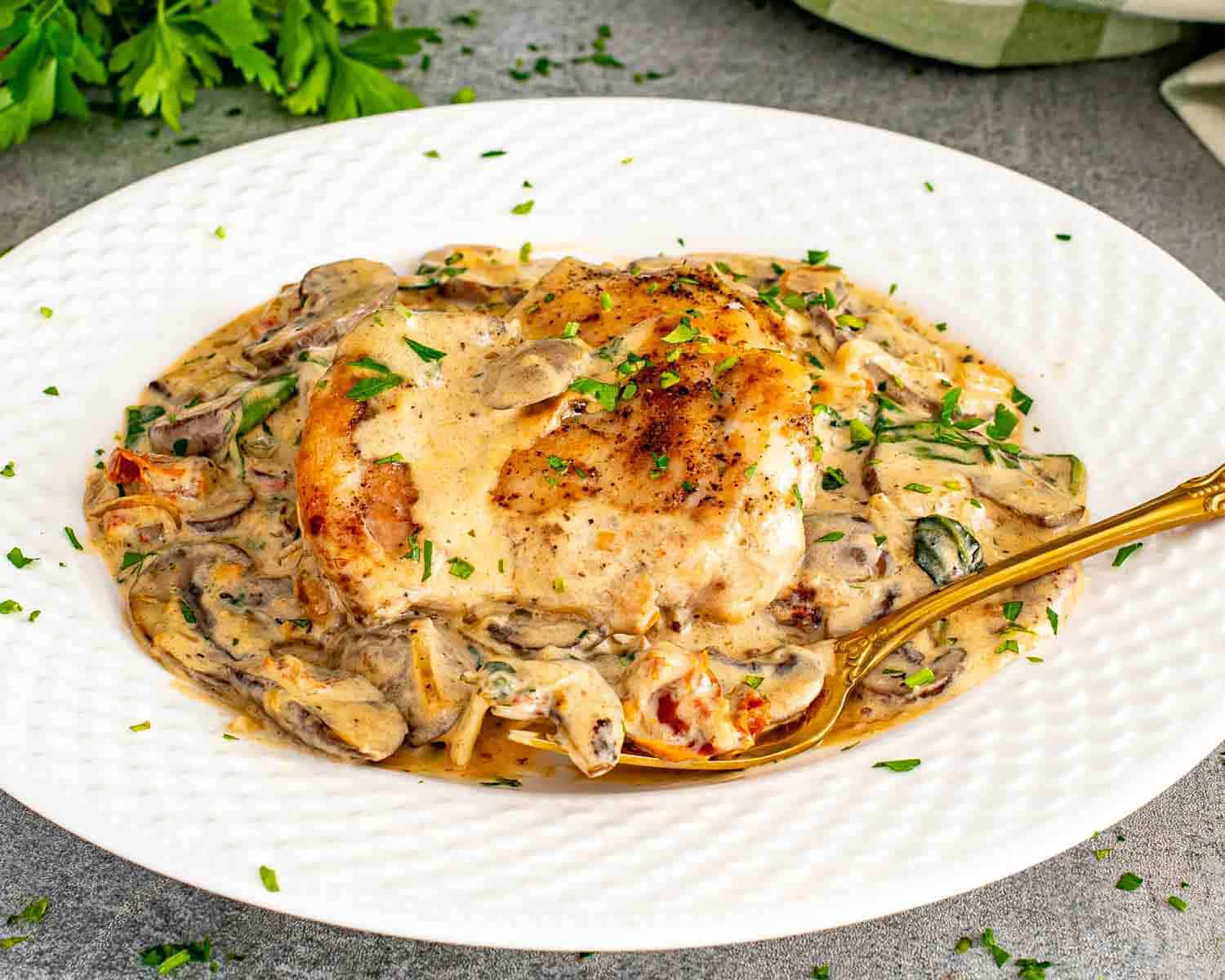 Creamy mushroom and sun dried tomato chicken served on white plate with golden seared chicken, mushrooms, spinach, and rich creamy sauce.