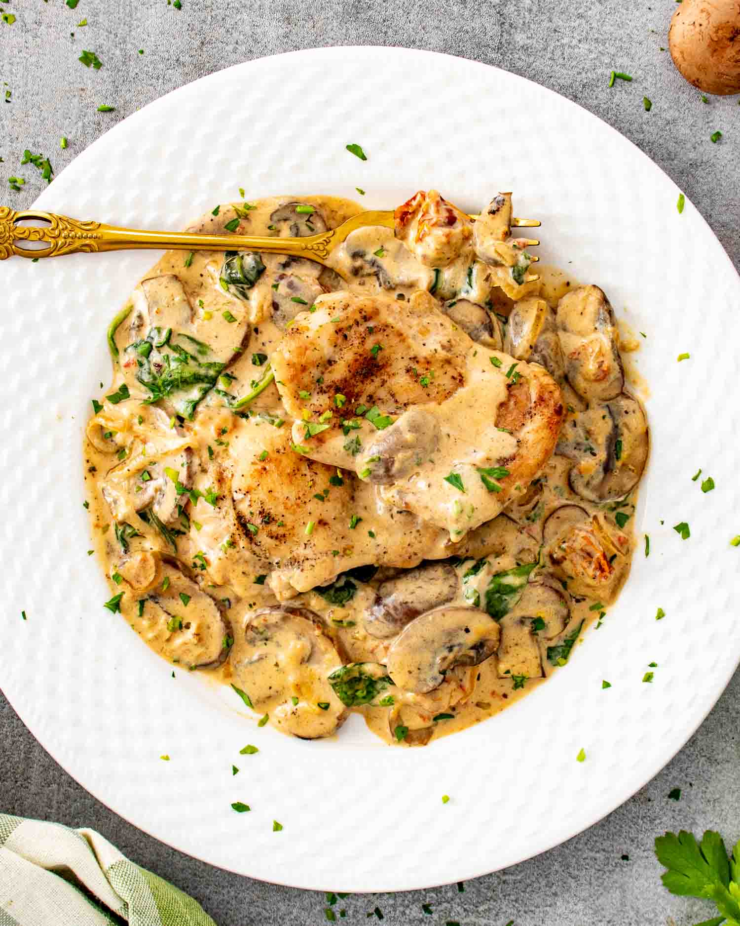 Creamy mushroom and sun dried tomato chicken served on white plate with golden seared chicken, mushrooms, spinach, and rich creamy sauce.