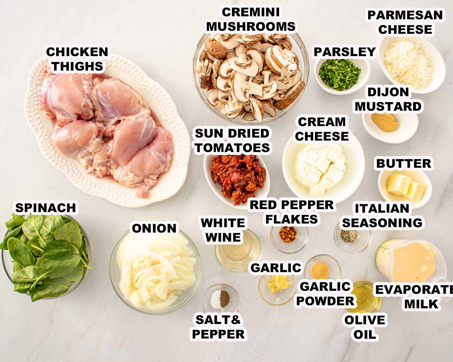 Ingredients for creamy mushroom and sun dried tomato chicken including chicken thighs, mushrooms, spinach, cream cheese, Parmesan, and seasonings arranged on countertop.
