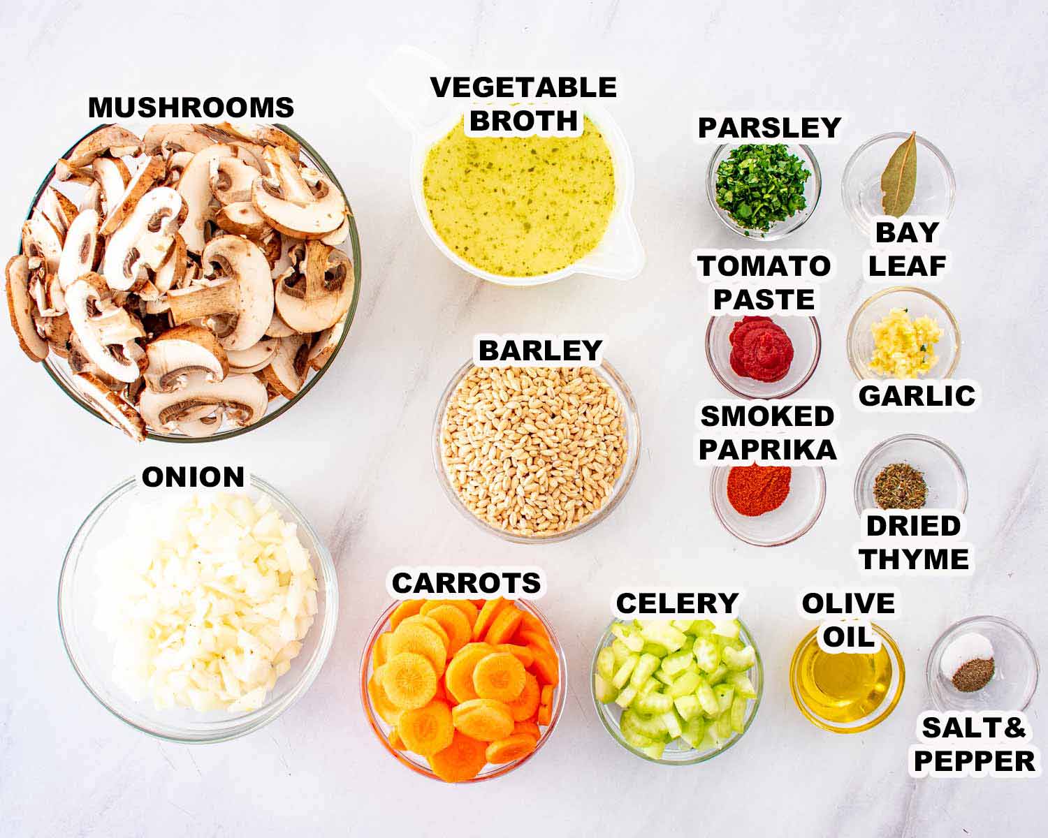Ingredients for mushroom barley soup including mushrooms, barley, carrots, celery, onion, garlic, herbs, and vegetable broth neatly arranged.