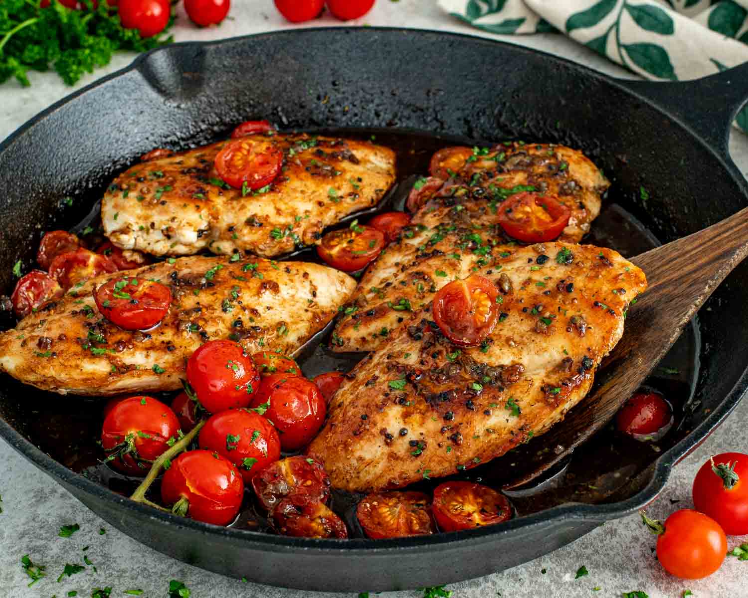 Juicy balsamic chicken breasts simmered in a cast iron skillet with blistered cherry tomatoes and fresh parsley garnish.