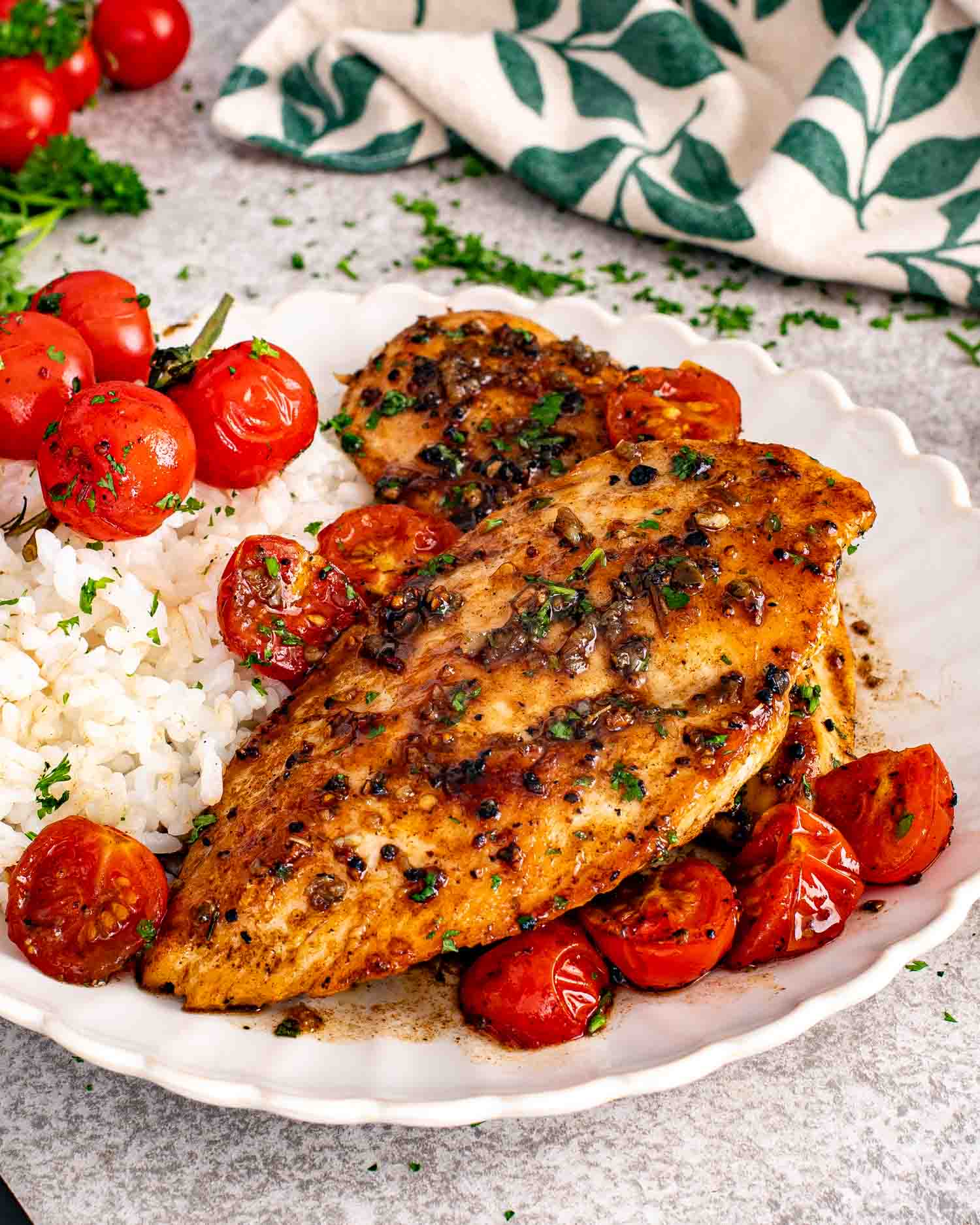 Tender balsamic chicken plated with white rice, roasted cherry tomatoes, and fresh parsley in a creamy scalloped serving bowl.