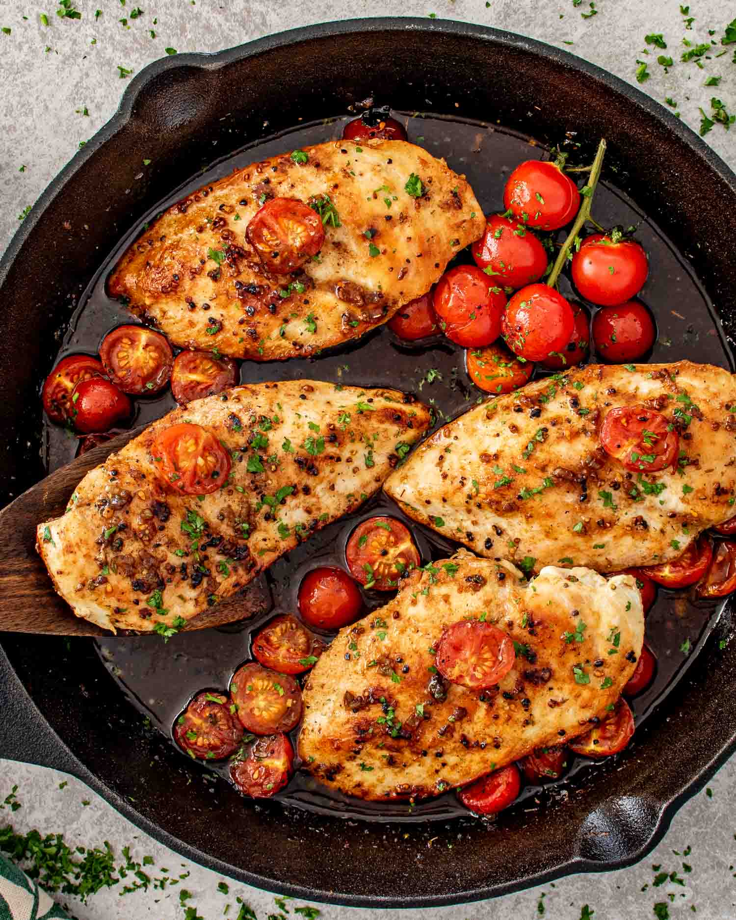Four balsamic chicken breasts cooking in a cast iron skillet surrounded by blistered cherry tomatoes and rich pan sauce.