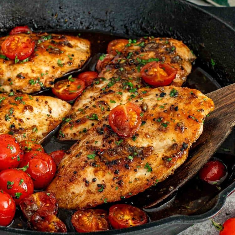 Juicy balsamic chicken breasts simmered in a cast iron skillet with blistered cherry tomatoes and fresh parsley garnish.