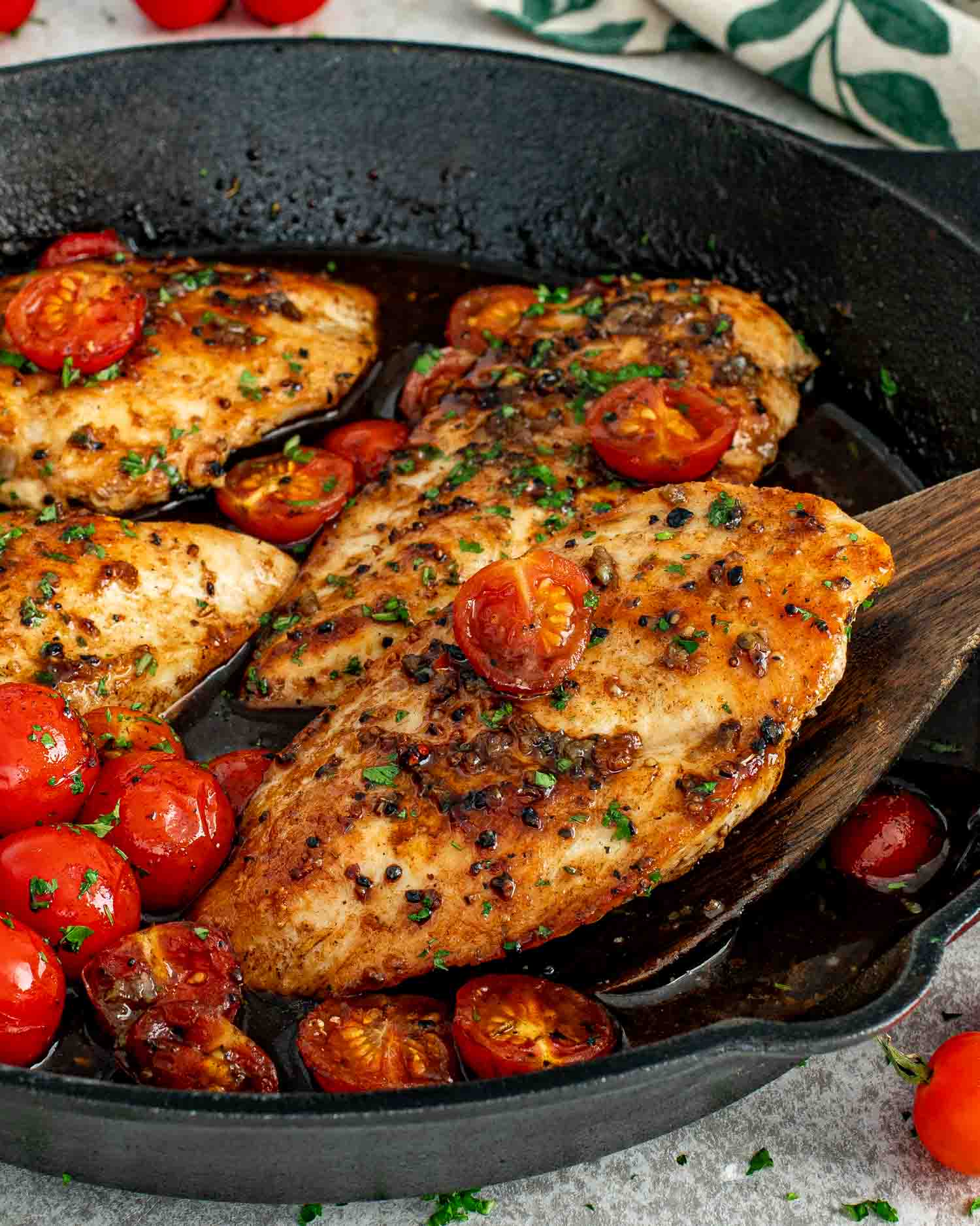 Juicy balsamic chicken breasts simmered in a cast iron skillet with blistered cherry tomatoes and fresh parsley garnish.