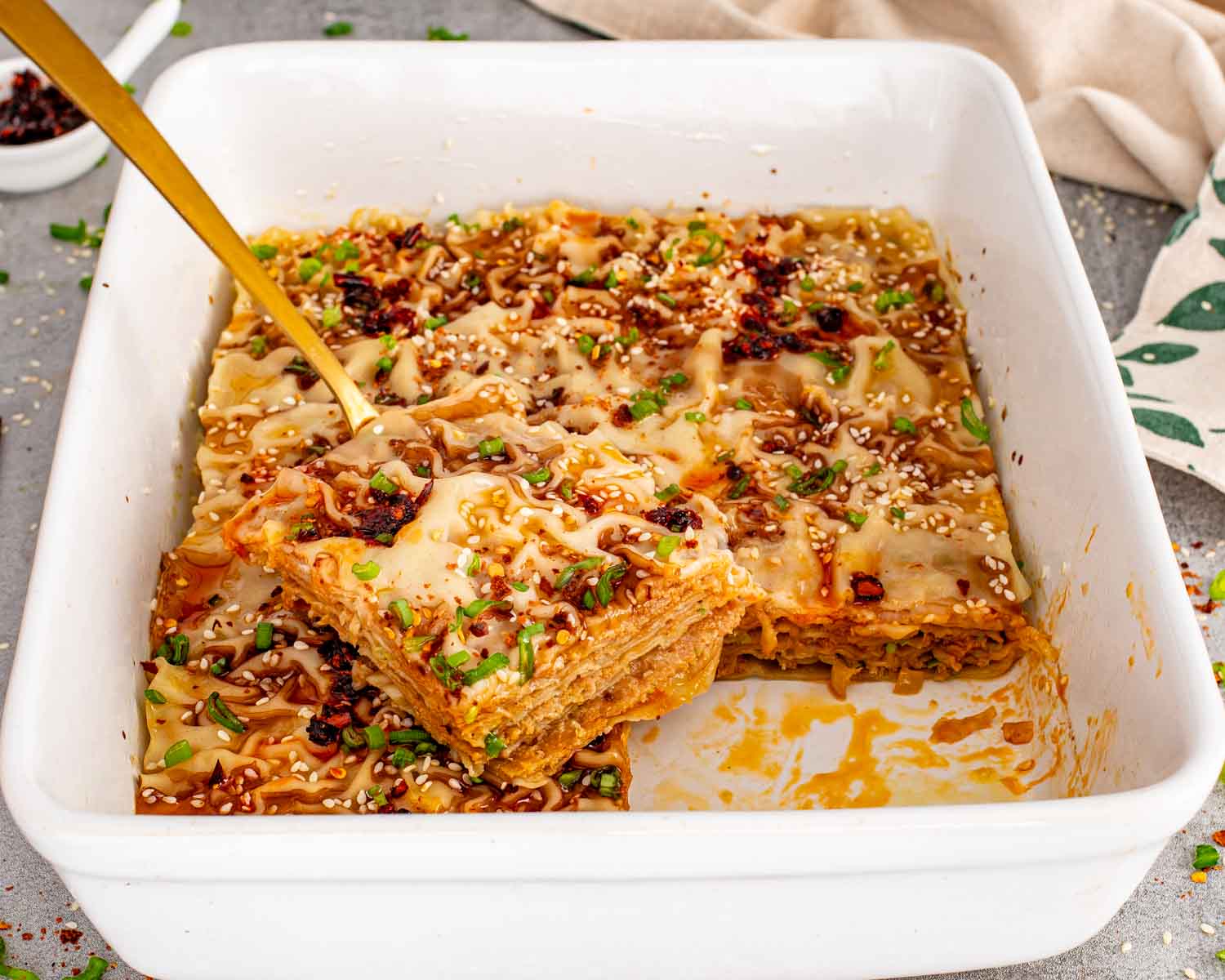 Top view of a white casserole dish filled with golden brown dumpling lasagna, garnished with green onions and sesame seeds.