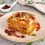 Close up view of a layered dumpling lasagna square on a vintage patterned plate with chili oil on the side.