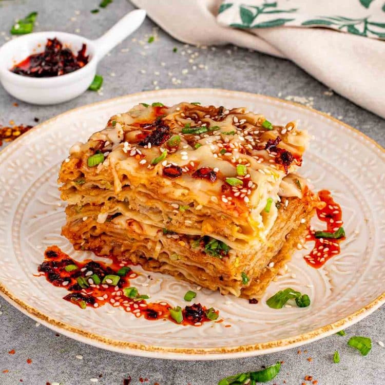 Close up view of a layered dumpling lasagna square on a vintage patterned plate with chili oil on the side.