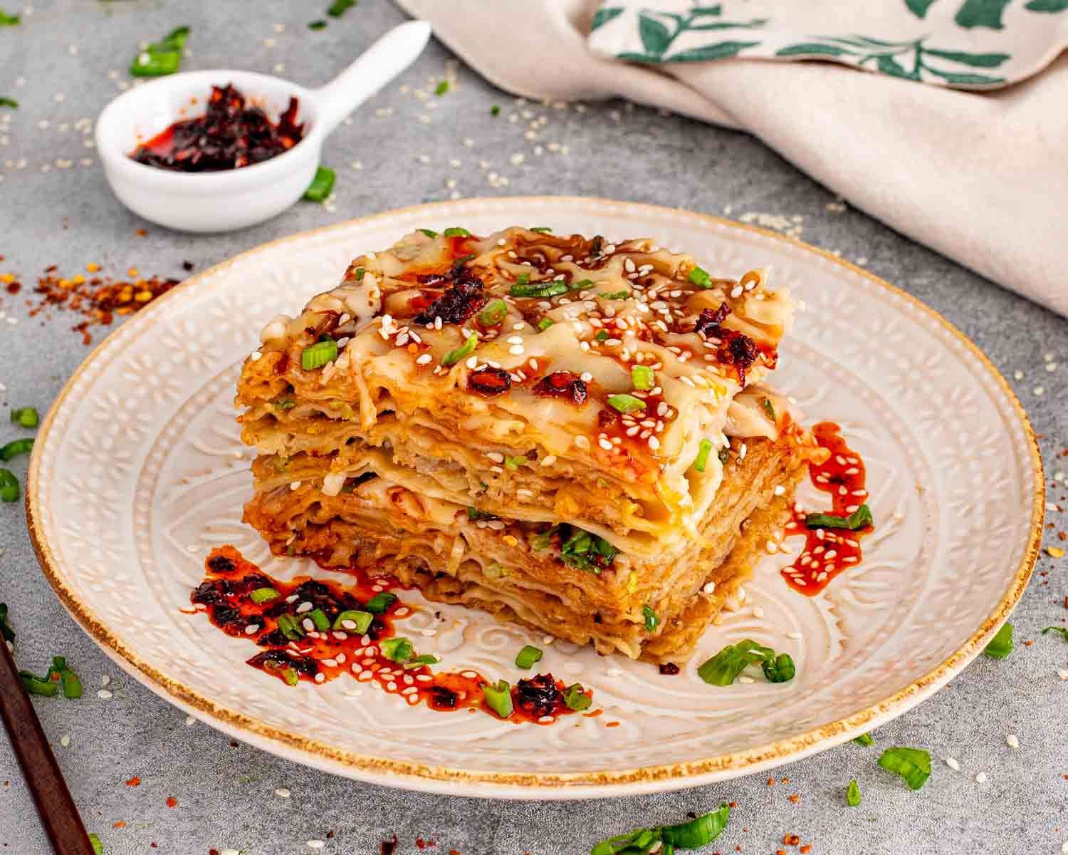 Close up view of a layered dumpling lasagna square on a vintage patterned plate with chili oil on the side.