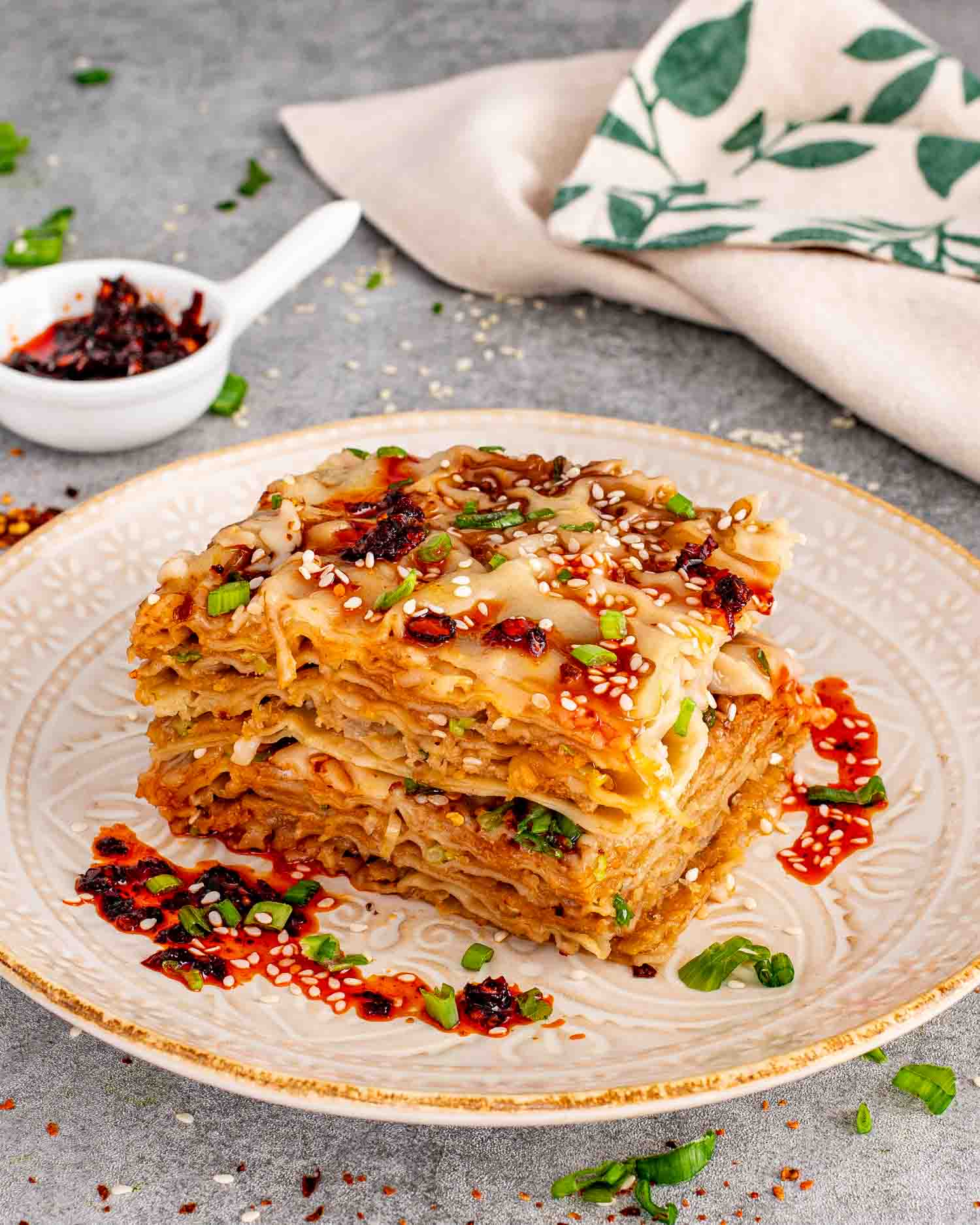 Close up view of a generous slice of layered dumpling lasagna on a decorative plate with chili crisp drizzle.