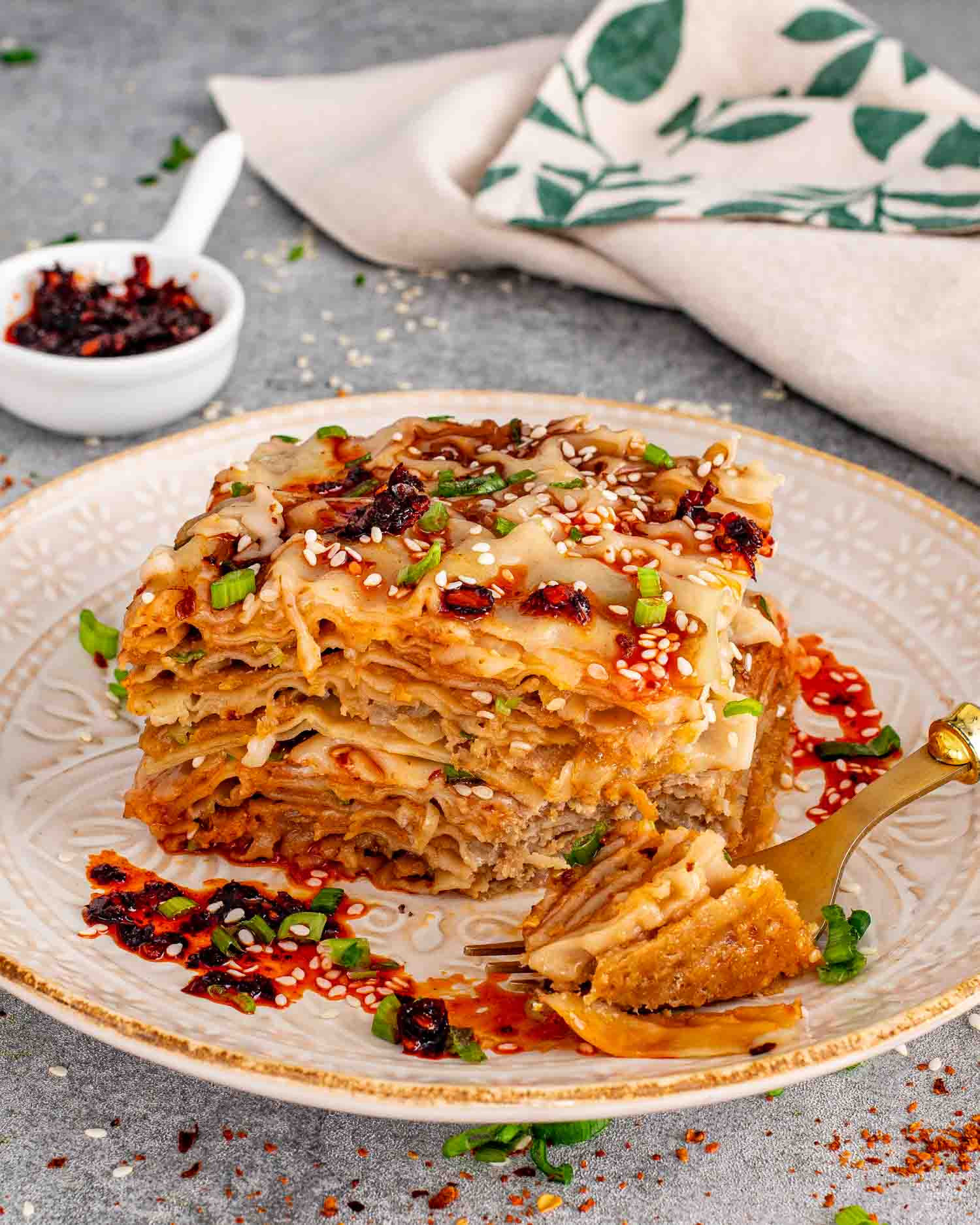 Close up view of a generous slice of layered dumpling lasagna on a decorative plate with chili crisp drizzle.