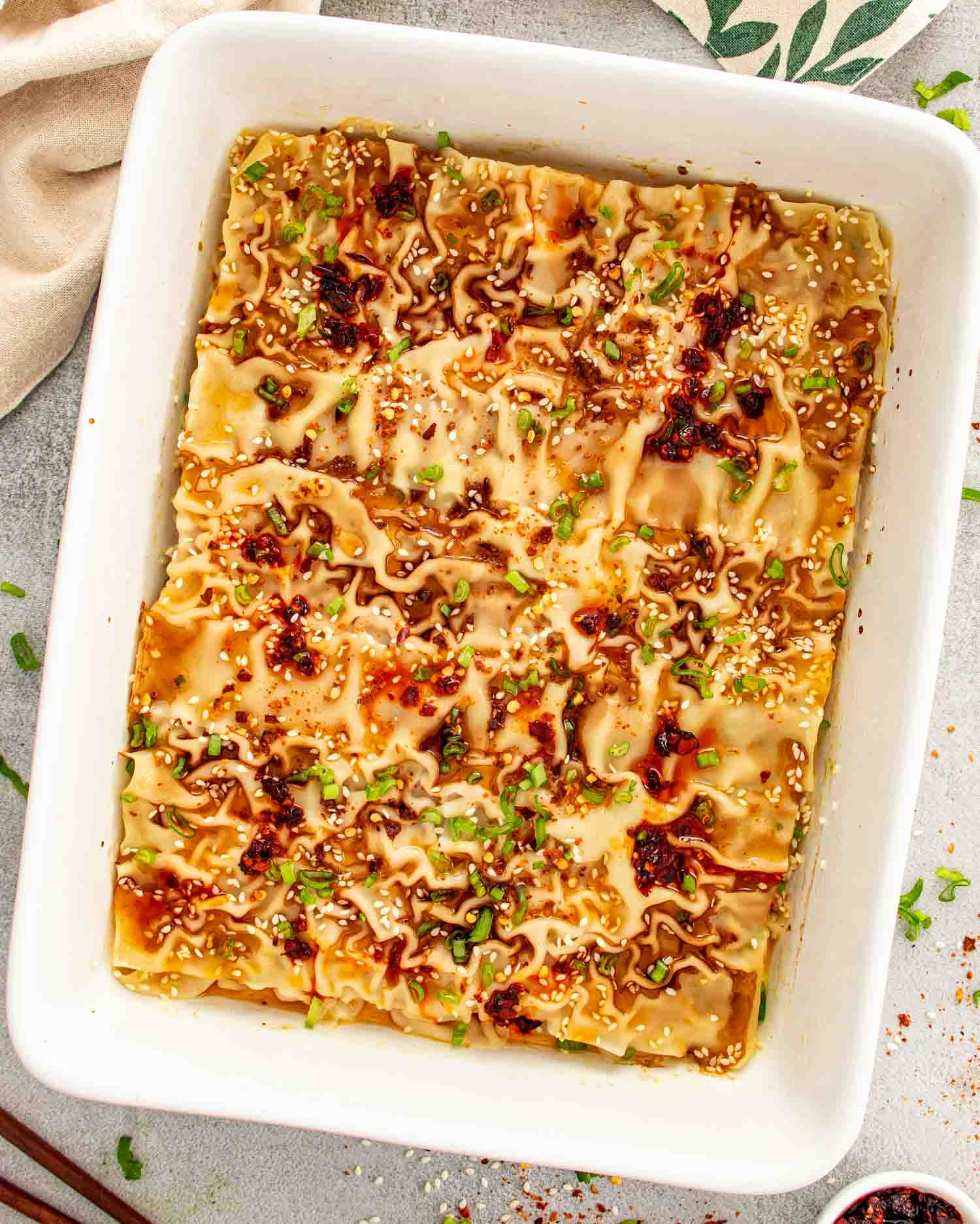 Top view of a white casserole dish filled with golden brown dumpling lasagna, garnished with green onions and sesame seeds.