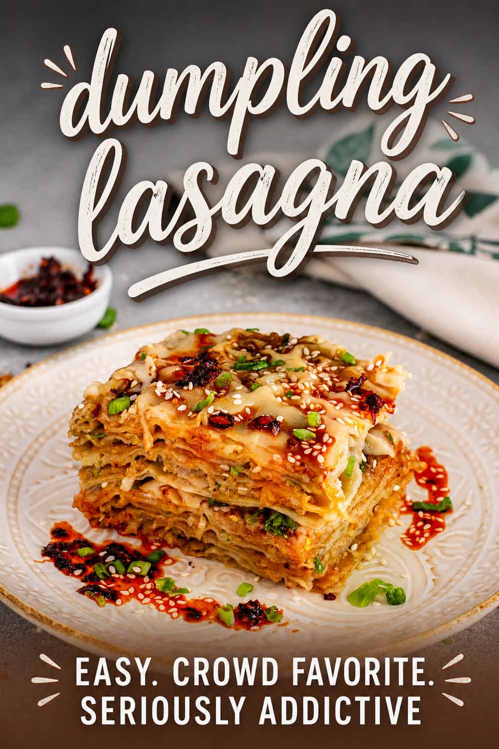 A single square of dumpling lasagna served on a white plate and topped with chili crisp, sesame seeds, and chives.