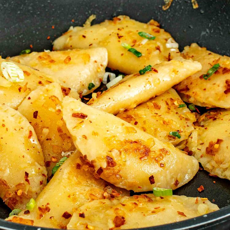 Golden pan fried homemade pierogi with caramelized onions and chili flakes in a black nonstick skillet.