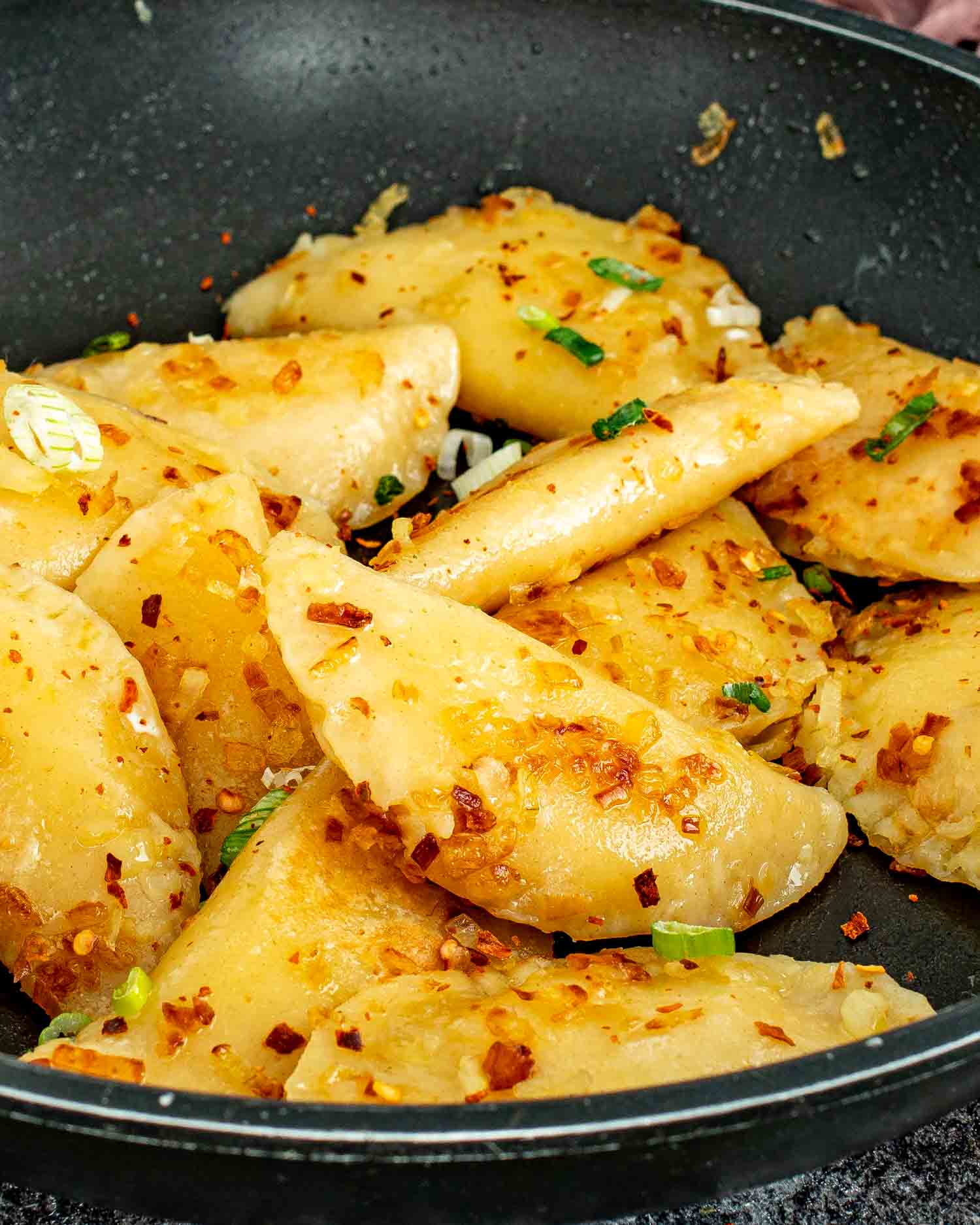 Golden pan fried homemade pierogi with caramelized onions and chili flakes in a black nonstick skillet.