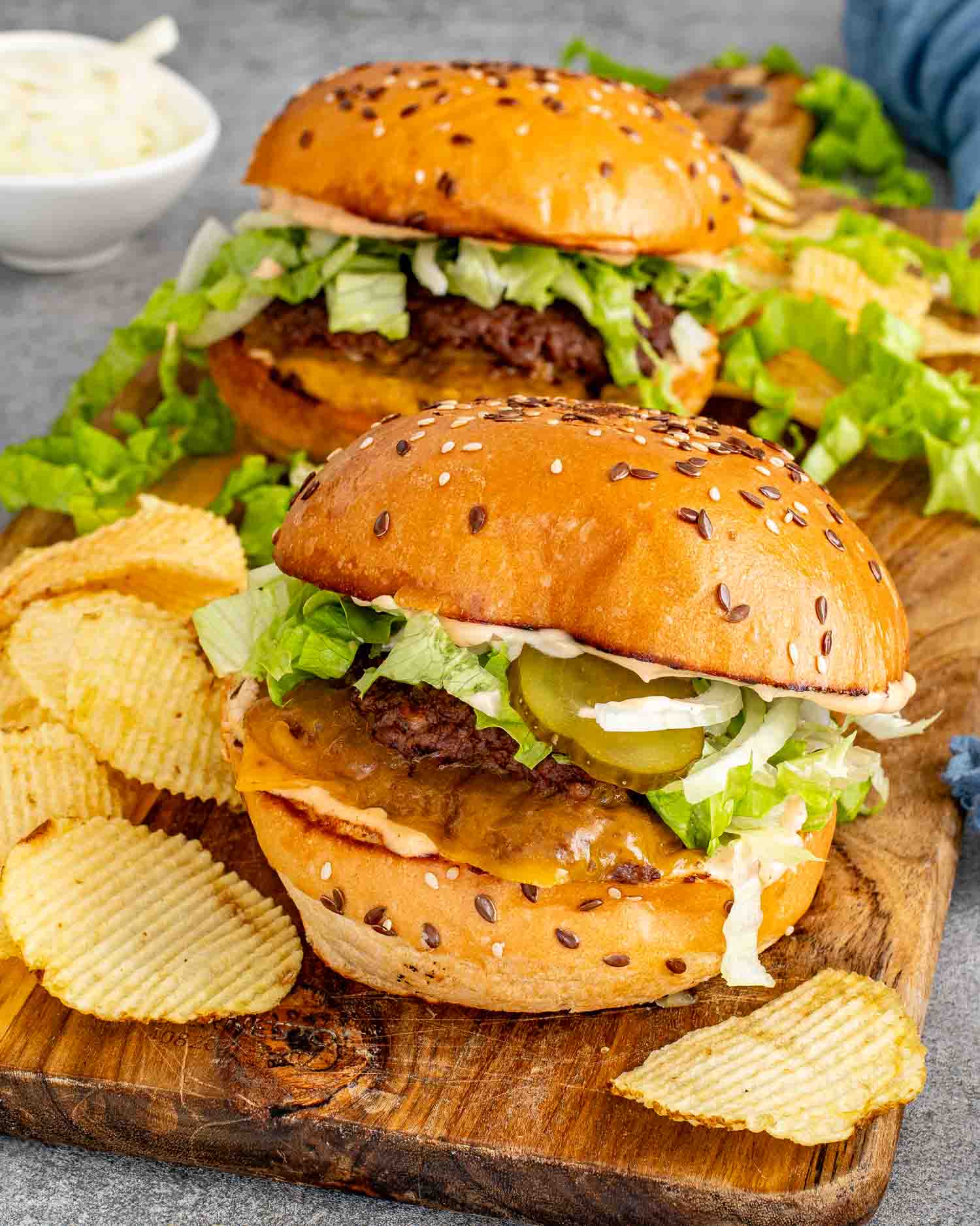 Two double smashed burgers loaded with cheddar cheese, special sauce, shredded lettuce, pickles, and onion on toasted sesame seed buns with ridged chips on a w