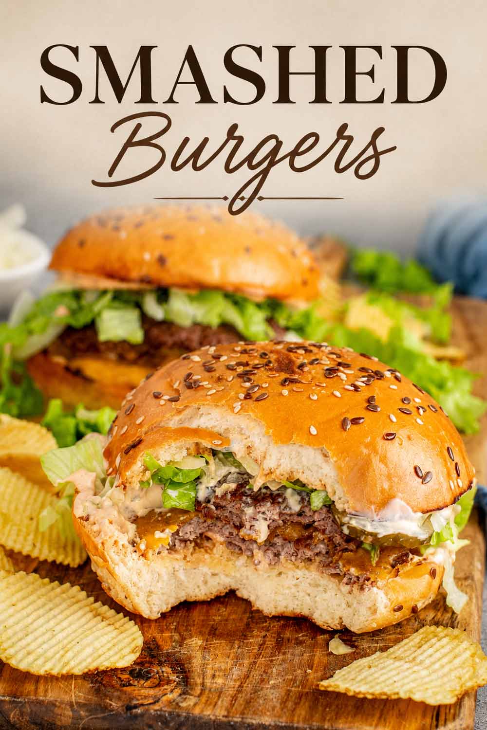 Smashed burger with a bite taken out showing the double patty and melted cheese on a wood board with chips and text overlay.