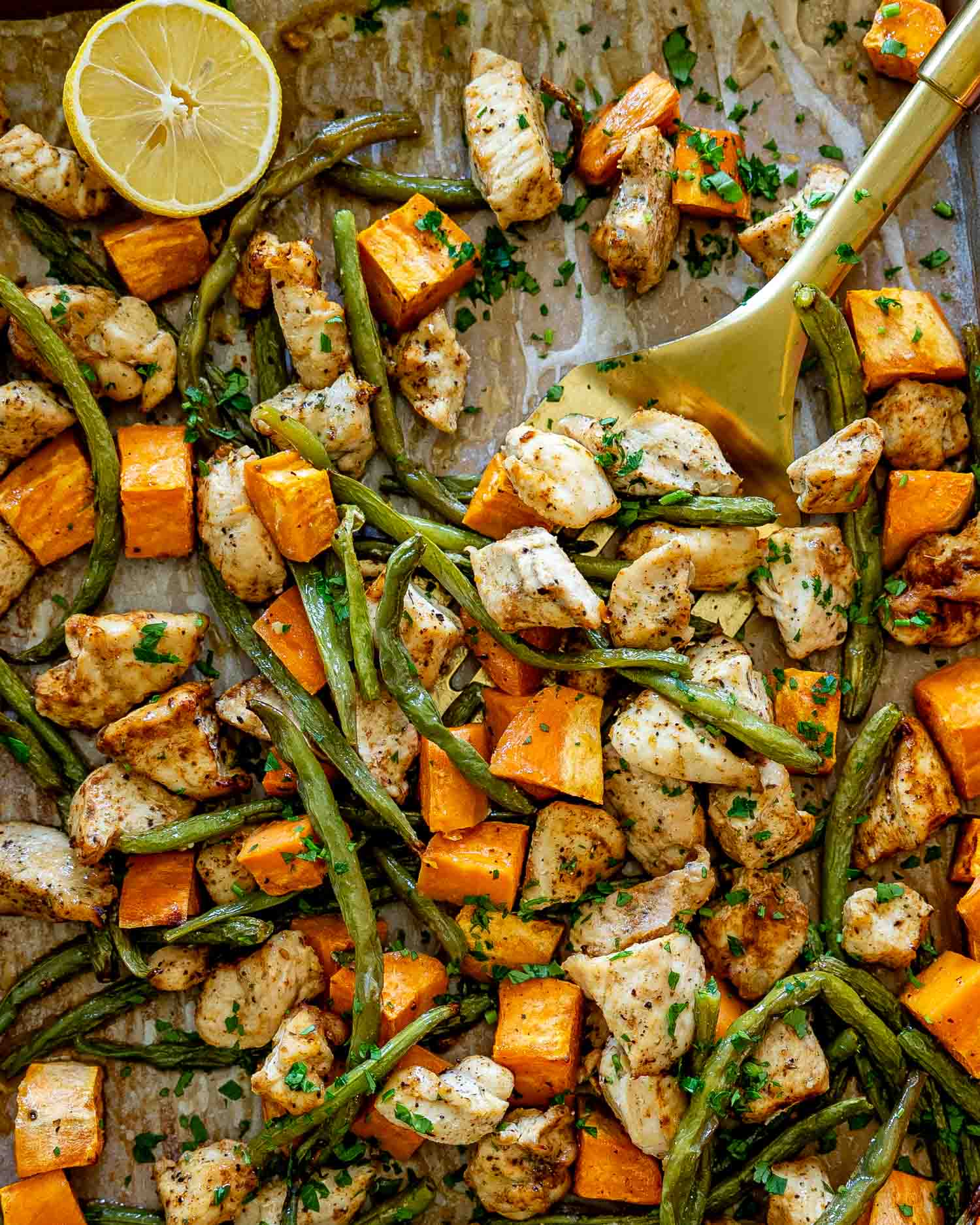 Overhead view of roasted chicken, green beans, and sweet potatoes spread across a baking sheet, ready for an easy family dinner.