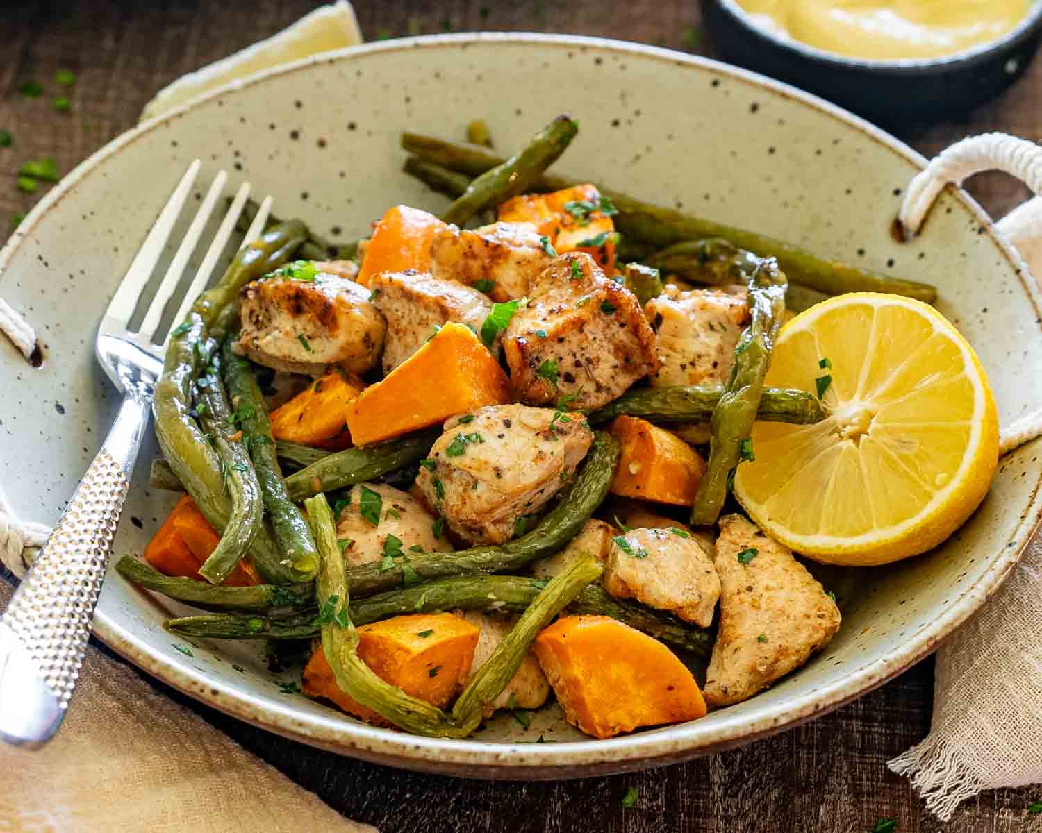 Close-up of juicy roasted chicken, tender green beans, and sweet potatoes served in a rustic bowl with fresh lemon.