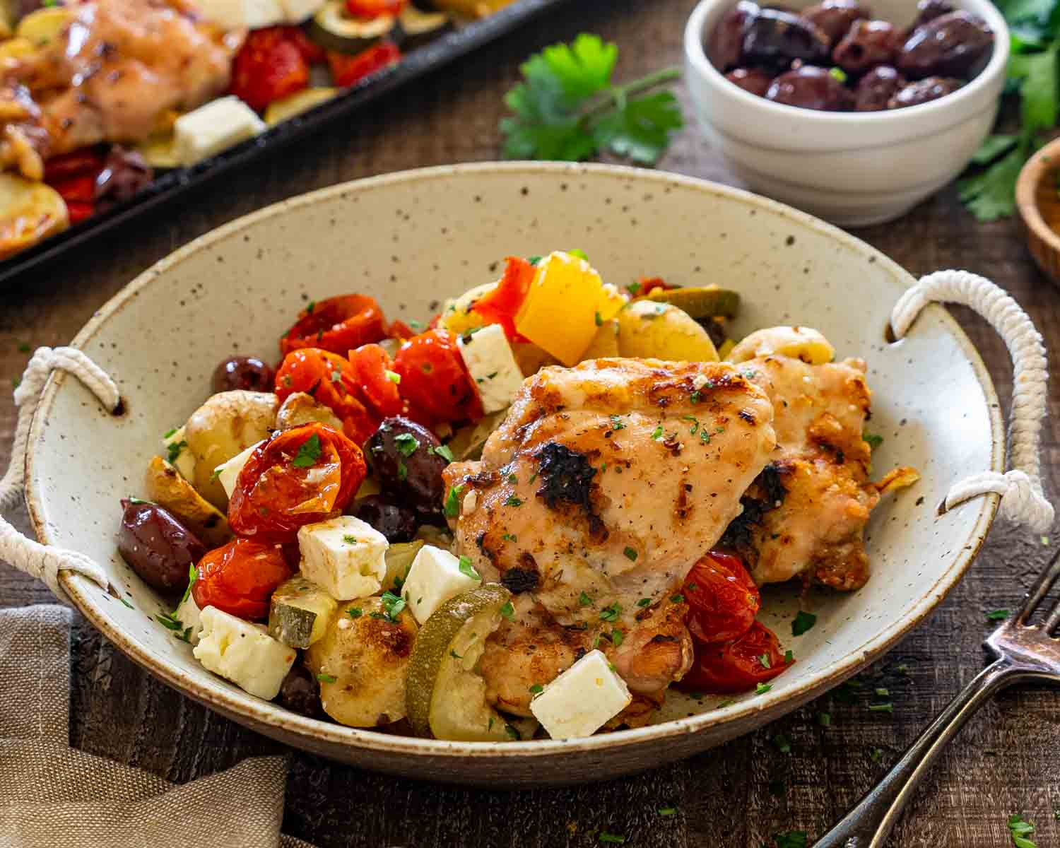 Rustic bowl filled with Greek chicken, roasted vegetables, potatoes, kalamata olives, feta cheese, and fresh parsley.