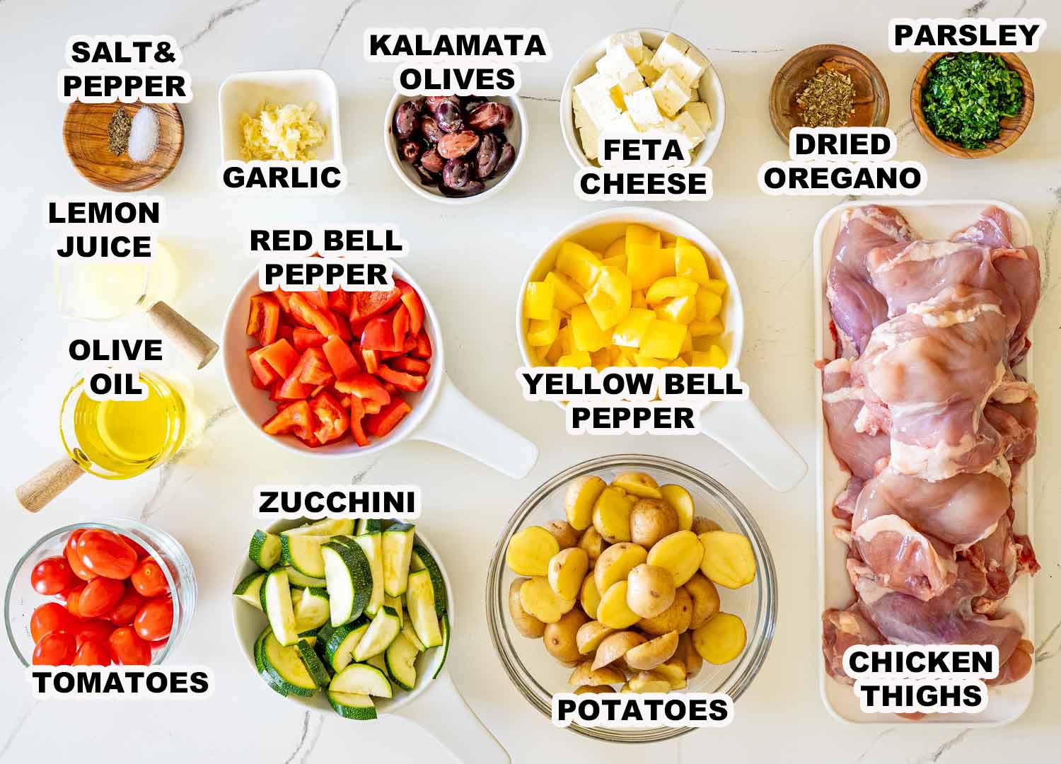 Ingredients for Greek sheet pan chicken including thighs, potatoes, zucchini, peppers, tomatoes, feta, olives, garlic, and herbs.