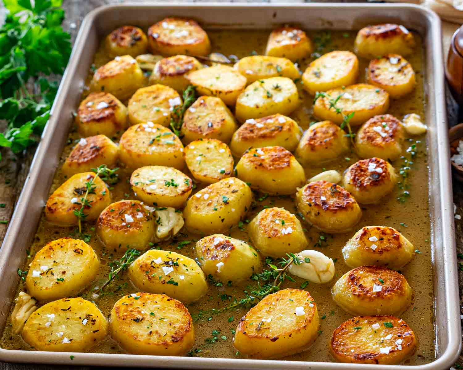 Whole sheet pan filled with golden melting potatoes roasting in buttery chicken broth with garlic, thyme, and flaky sea salt.