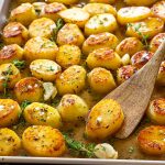 Close-up of buttery melting potatoes with caramelized tops, fresh thyme, garlic cloves, and rich pan juices ready for serving.