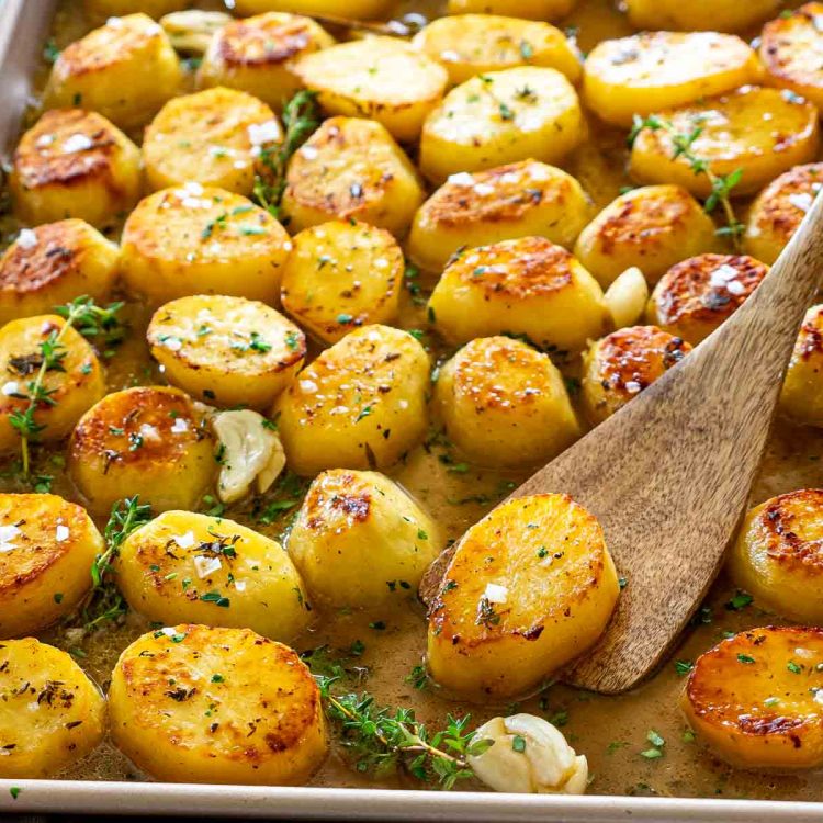 Close-up of buttery melting potatoes with caramelized tops, fresh thyme, garlic cloves, and rich pan juices ready for serving.