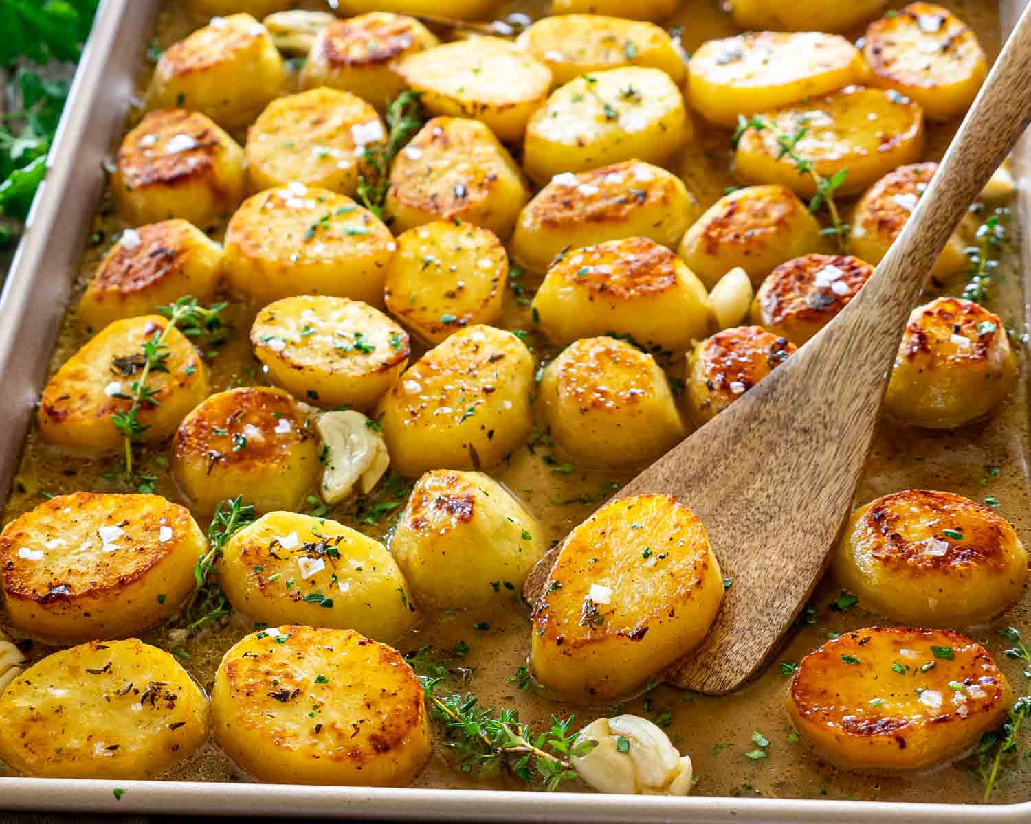 Close-up of buttery melting potatoes with caramelized tops, fresh thyme, garlic cloves, and rich pan juices ready for serving.