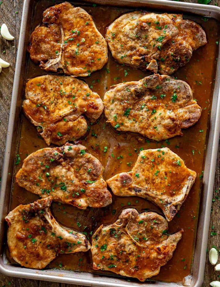 Sheet pan filled with oven baked honey garlic pork chops glazed with buttery garlic sauce and herbs.