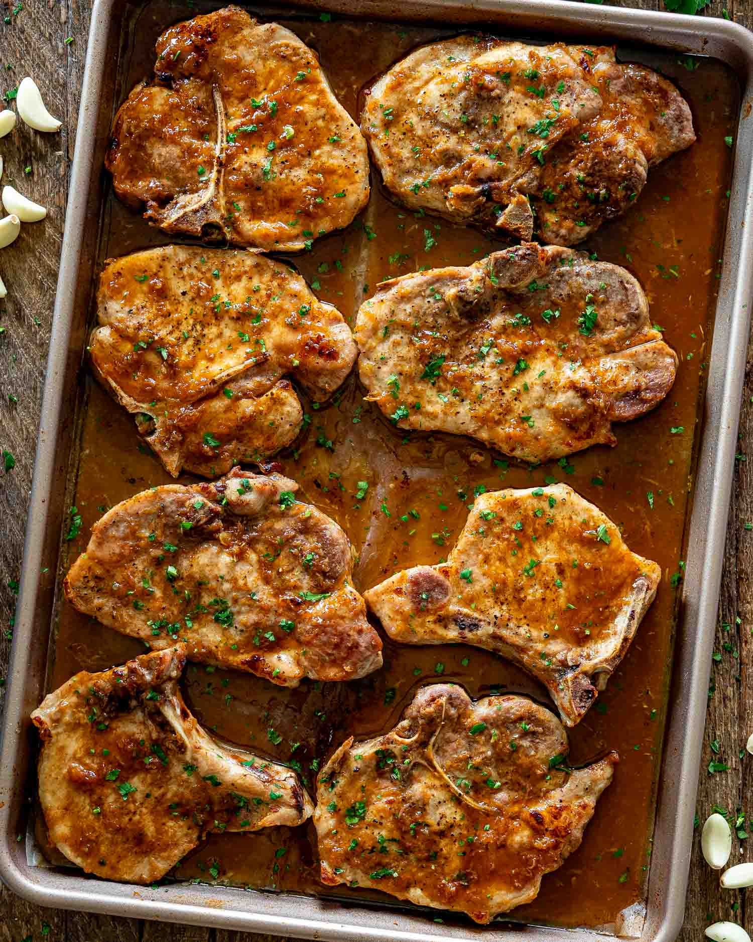 Sheet pan filled with oven baked honey garlic pork chops glazed with buttery garlic sauce and herbs.