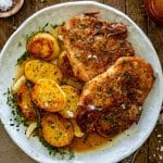 Honey garlic pork chops served with roasted potatoes, fresh thyme, garlic cloves, and savory pan juices.