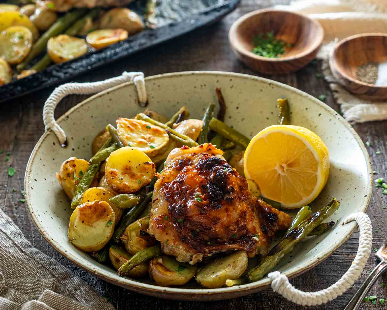 Single serving of Parmesan garlic chicken with roasted potatoes and green beans in rustic handled bowl with lemon.