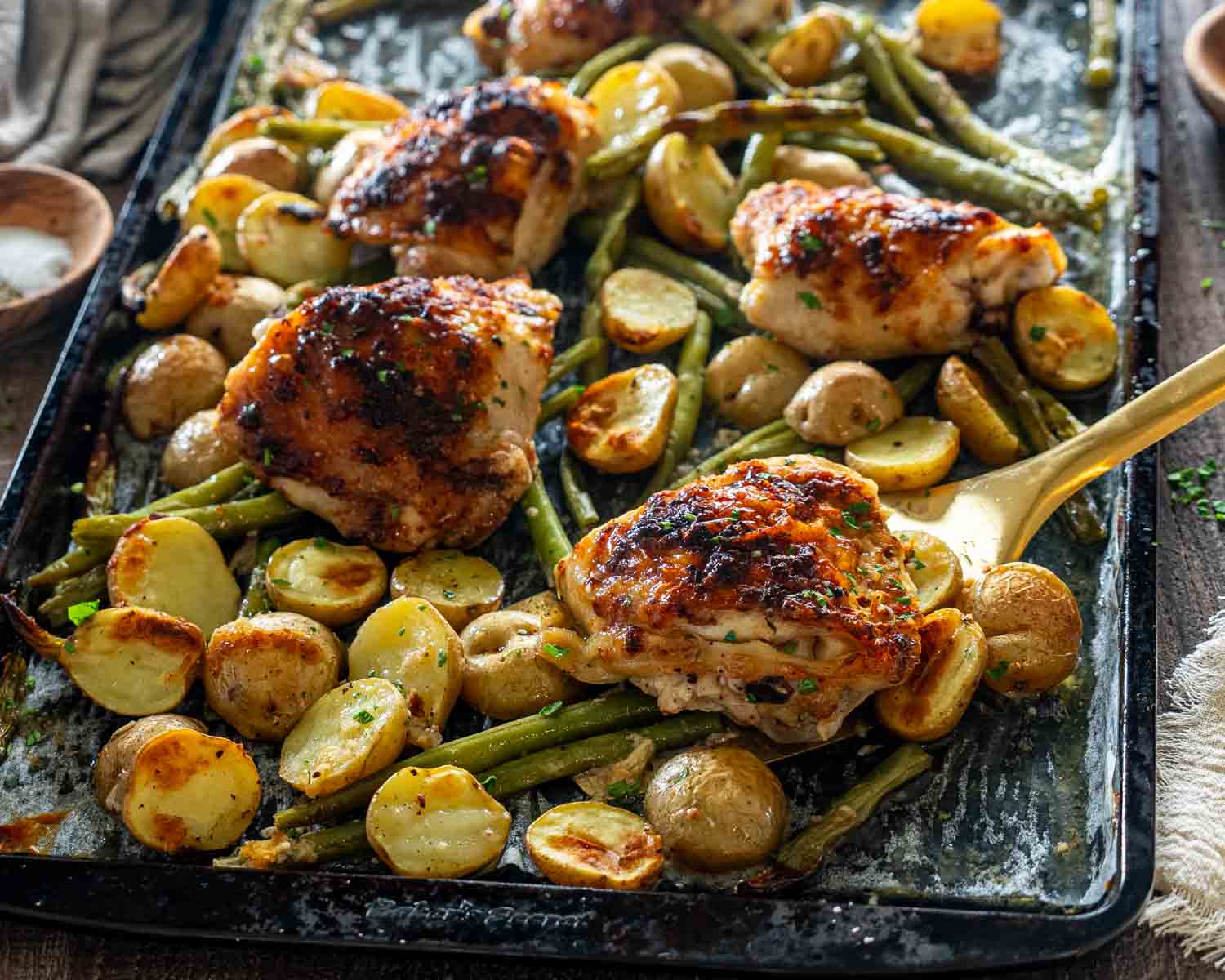 Golden Parmesan garlic chicken thighs surrounded by roasted potatoes and green beans on rustic sheet pan dinner.