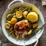 Rustic bowl filled with Parmesan garlic chicken, roasted baby potatoes, green beans, and fresh lemon on wooden table.